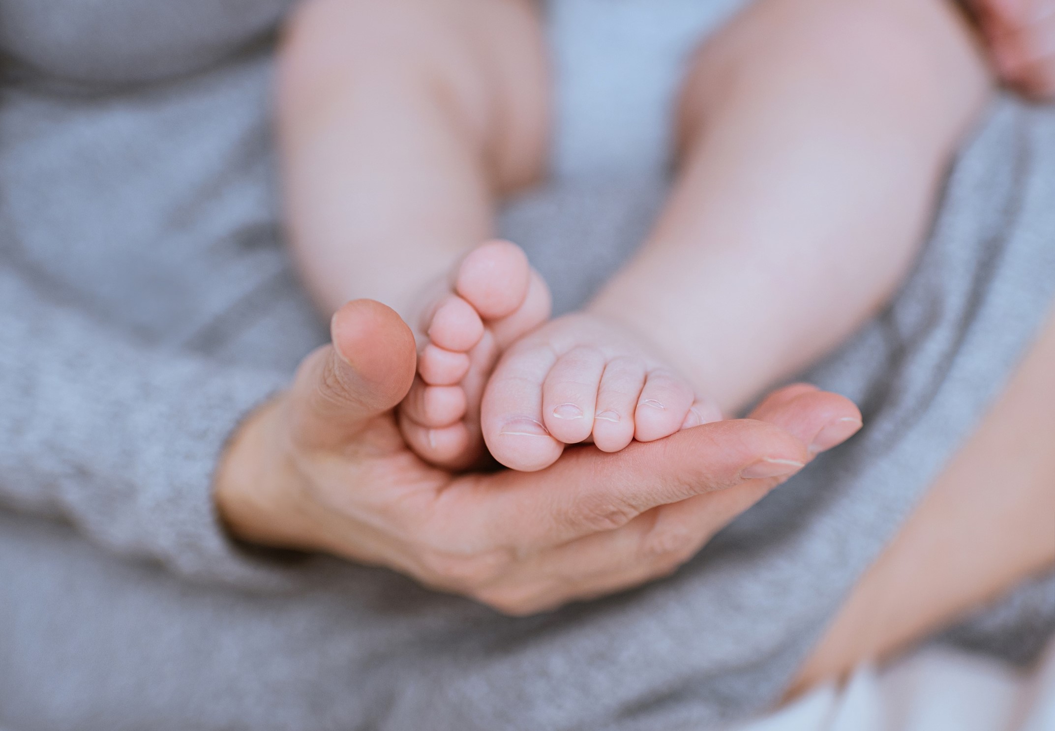 Image of a mom's hand holding baby's feet, which introduces the Birthing Stories section for the Firenze Moms 4 Moms Network